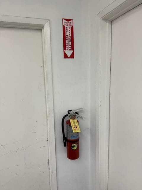 Smaller tagged ABC extinguisher mounted between two doors with a location sign above