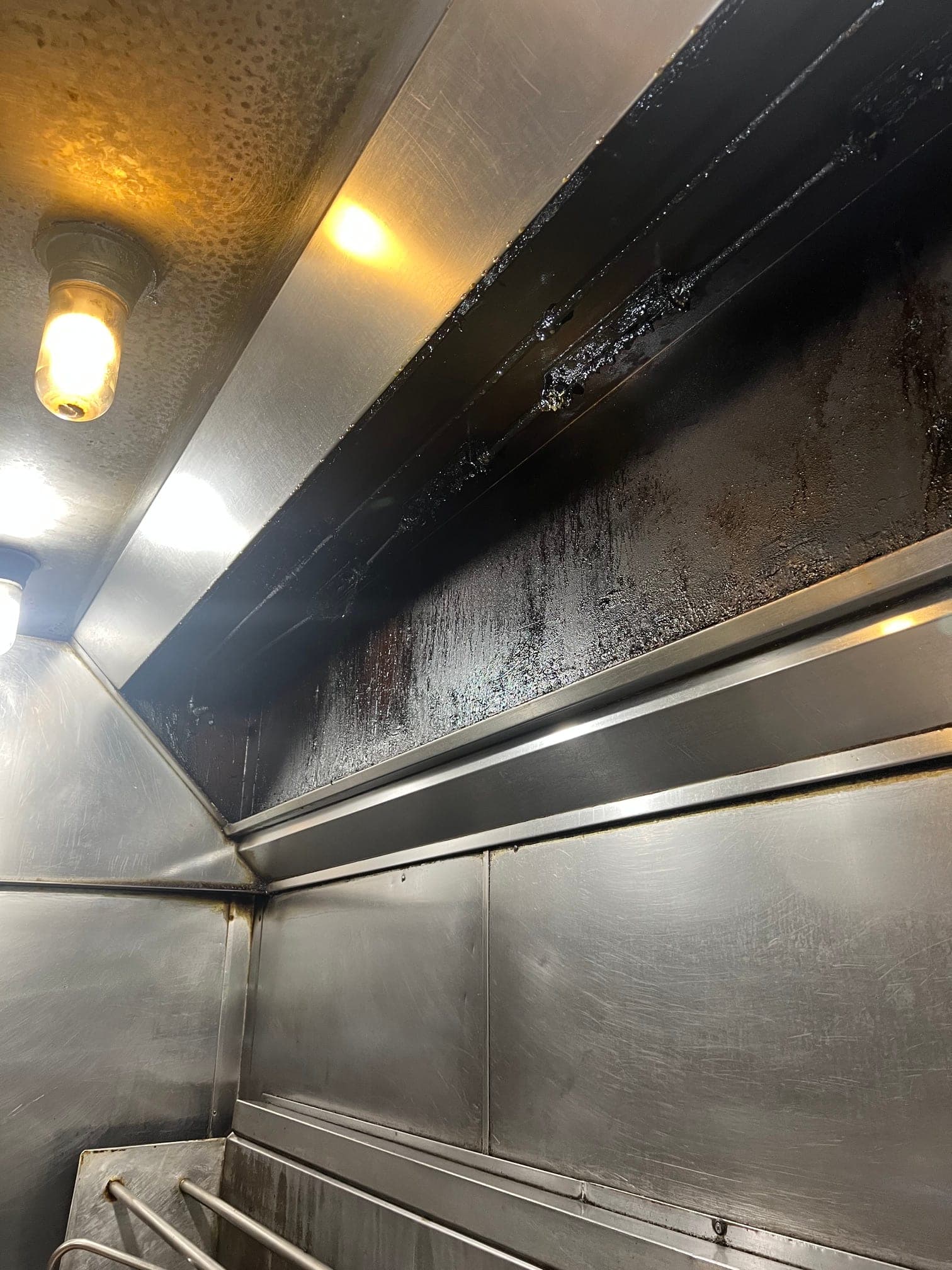 Stainless exhaust hood over a wok station, the hood wall streaked with grease