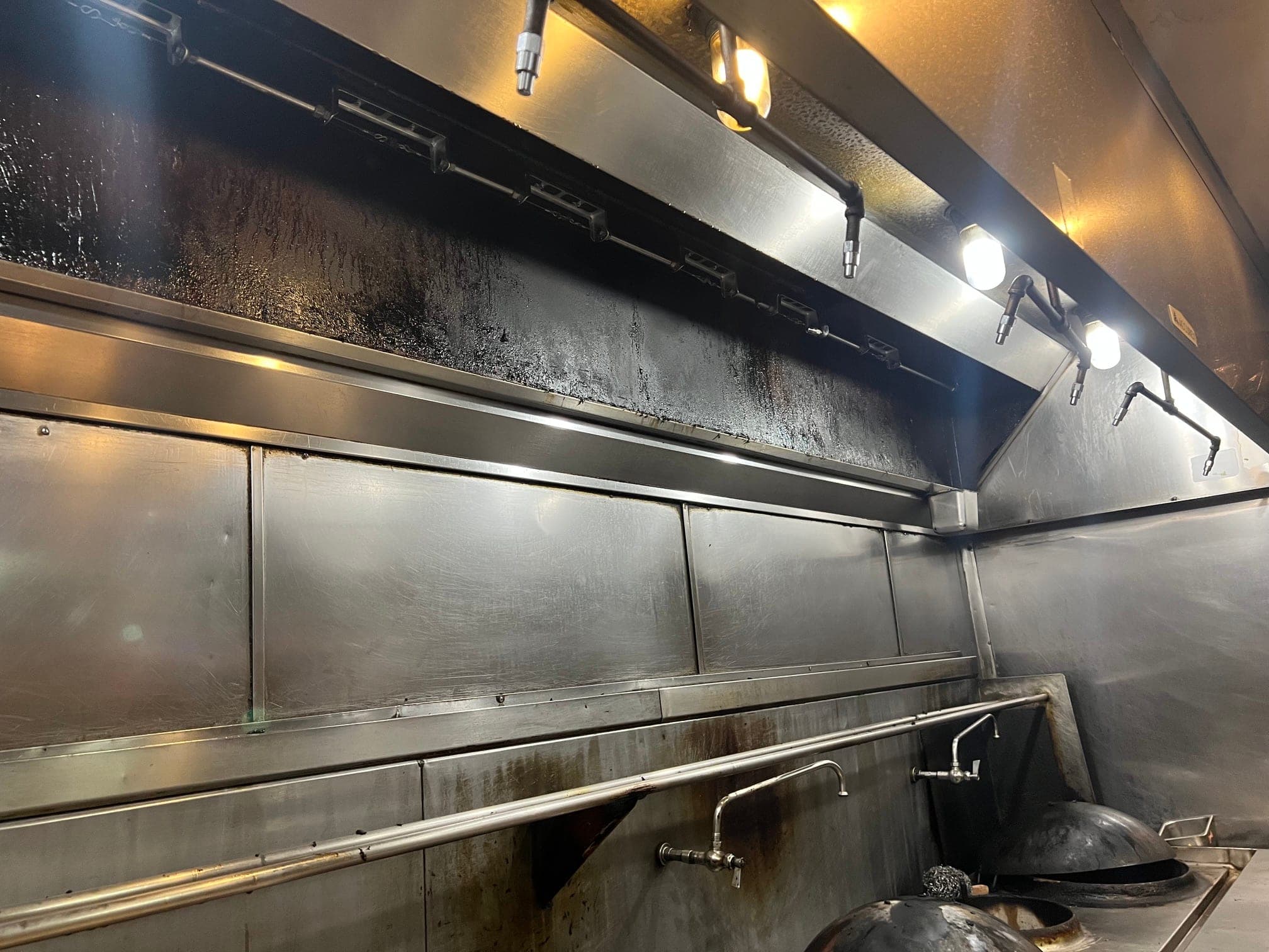 Detection line with brackets and fusible links running the length of the hood over the woks, nozzles above