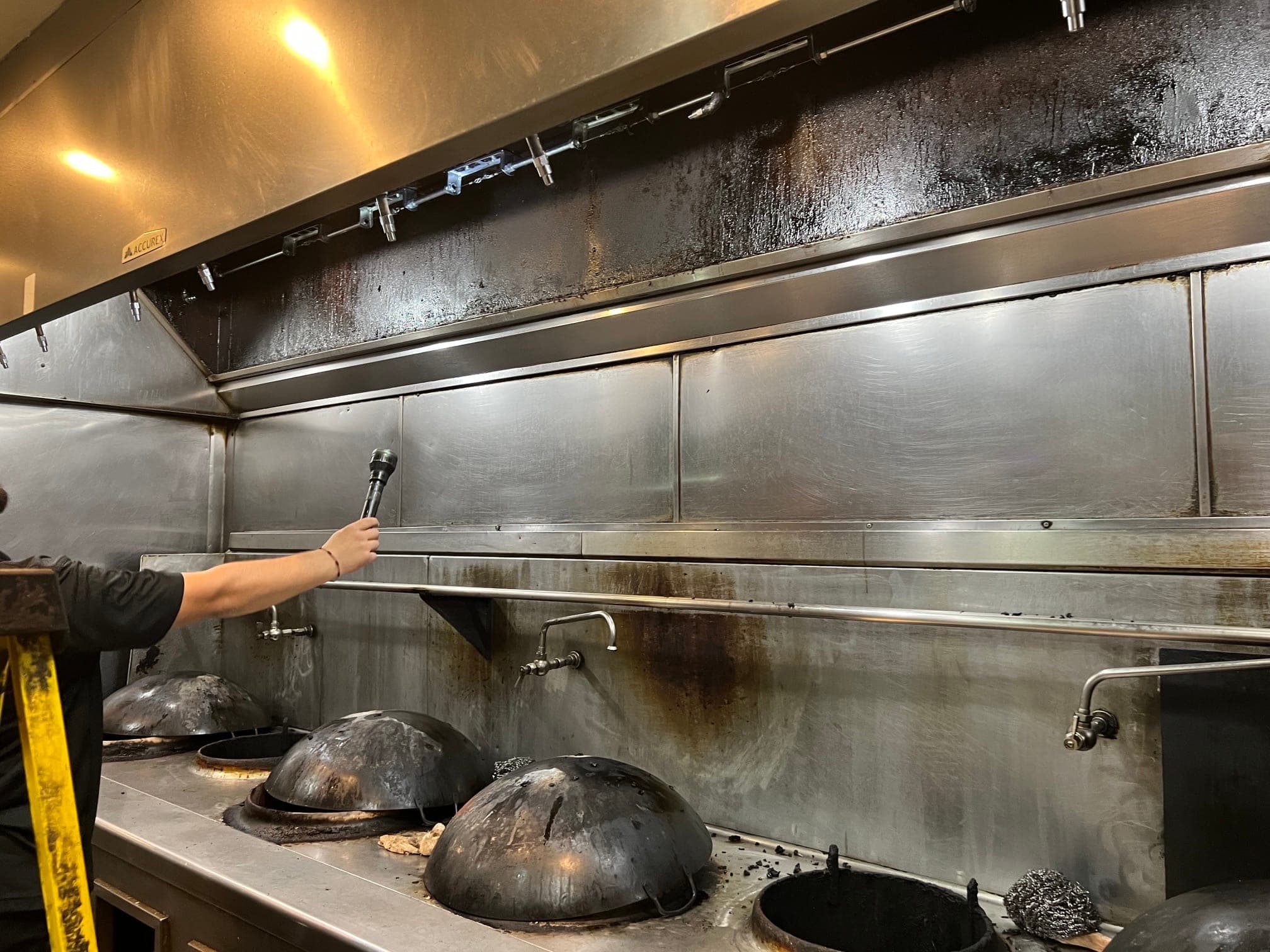 Technician's arm lighting the detection line inside the hood above a row of woks