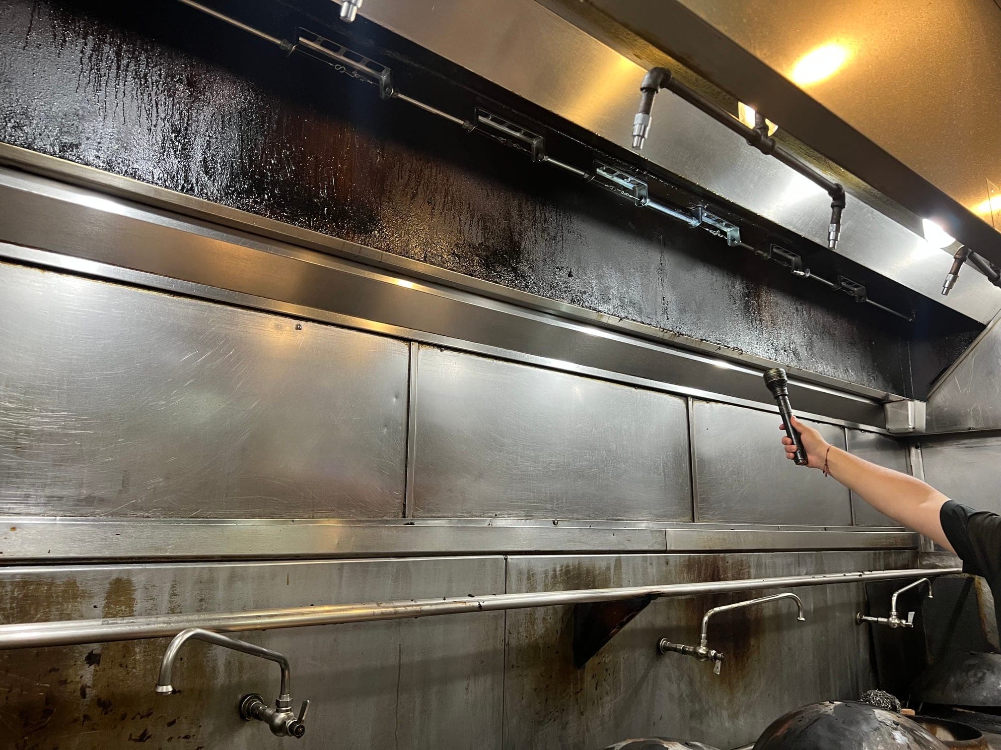 Technician inspecting nozzles and detection brackets along the full length of the wok hood